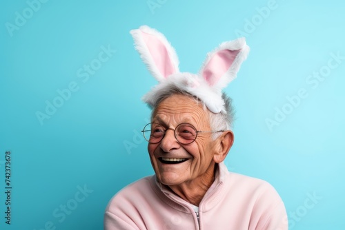 An elderly LGBTQ+ man, aged 70, wearing easter bunny ears and sharing a sweet moment together, against a muted pastel sky blue background, allowing space for Easter greetings or messages © Hanna Haradzetska