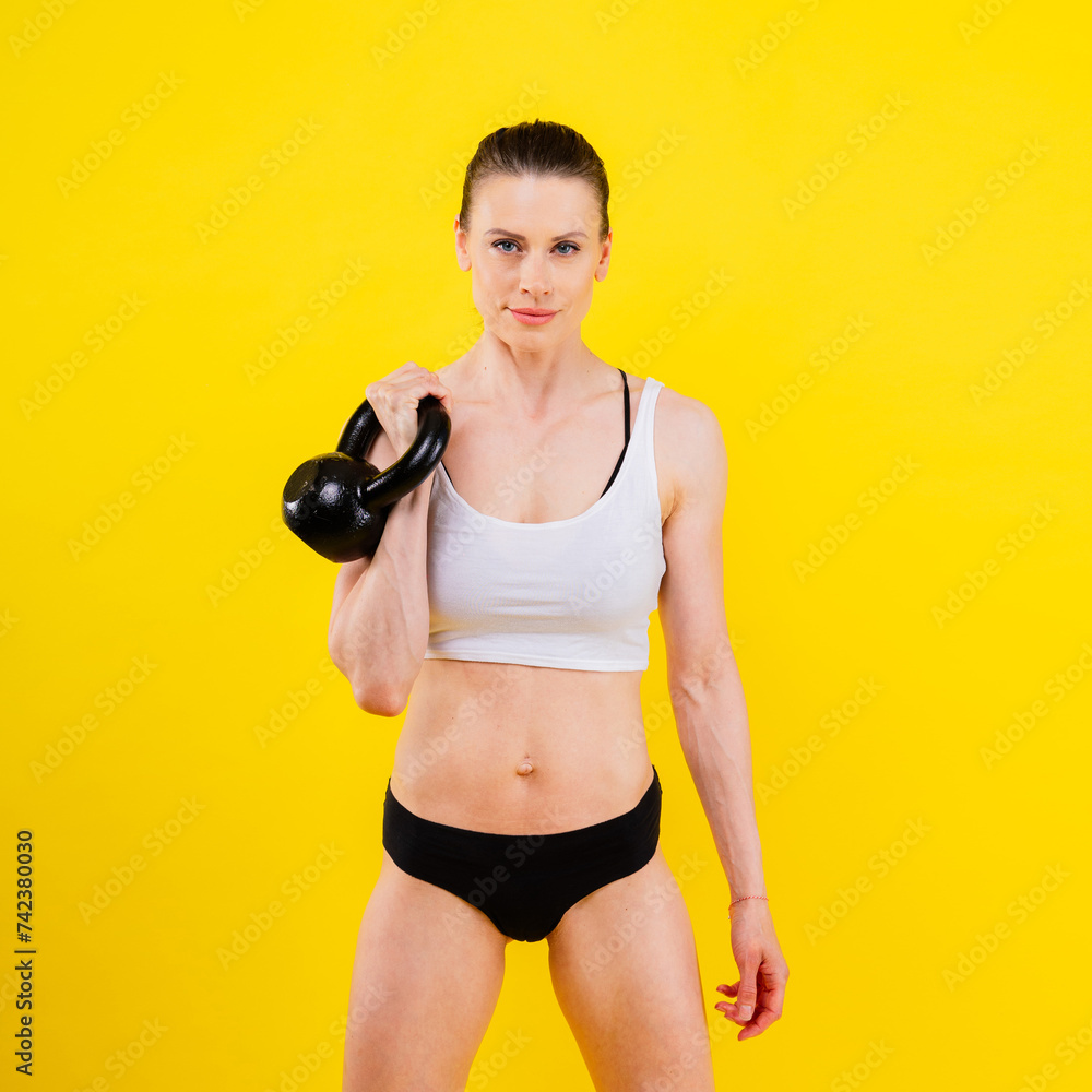 Woman in sportswear doing crossfit workout with kettle bell on dark yellow red background. Woman in sportswear doing crossfit workout with kettle bell on dark yellow red background.