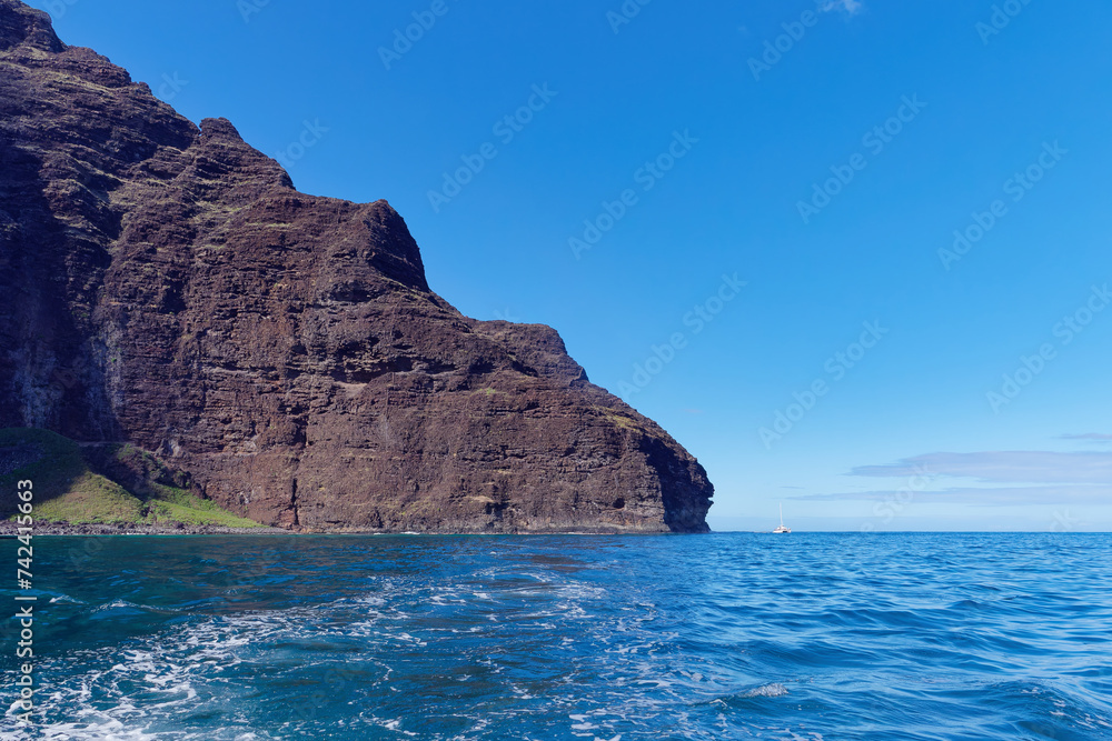 Magnificent cliff in the Pacific ocean and a small boat next to it view from a tourist boat at Napali Coast State Wilderness Park, Island of Kauai, Hawaii