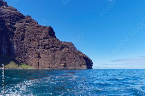Magnificent cliff in the Pacific ocean and a small boat next to it view from a tourist boat at Napali Coast State Wilderness Park, Island of Kauai, Hawaii