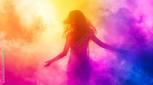A young woman with long hair and spread arms dances in a cloud of multi-colored powder and falling light. Celebrating the traditional Indian spring festival Holi