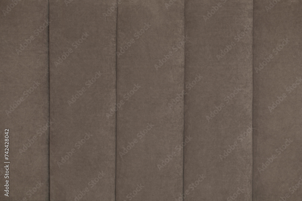 Fototapeta premium A soft wall in the form of stripes is covered with plush velor fabric in light brown shades. Background of decorative soft quilted surface made of furniture fabric with small fibers close-up.