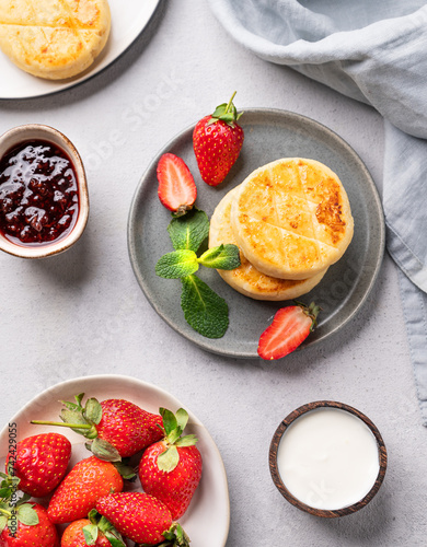 Fototapeta Naklejka Na Ścianę i Meble -  Cottage cheese, cheesecakes or syrniki with strawberries, sour cream, berry jam and mint leaves on a gray plate on a light background with napkin.