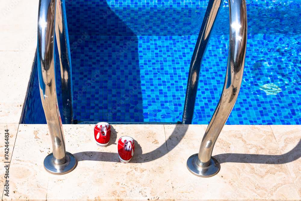 Metal chrome railings, pool ladder for safe entry into the water, and red kids shoes.