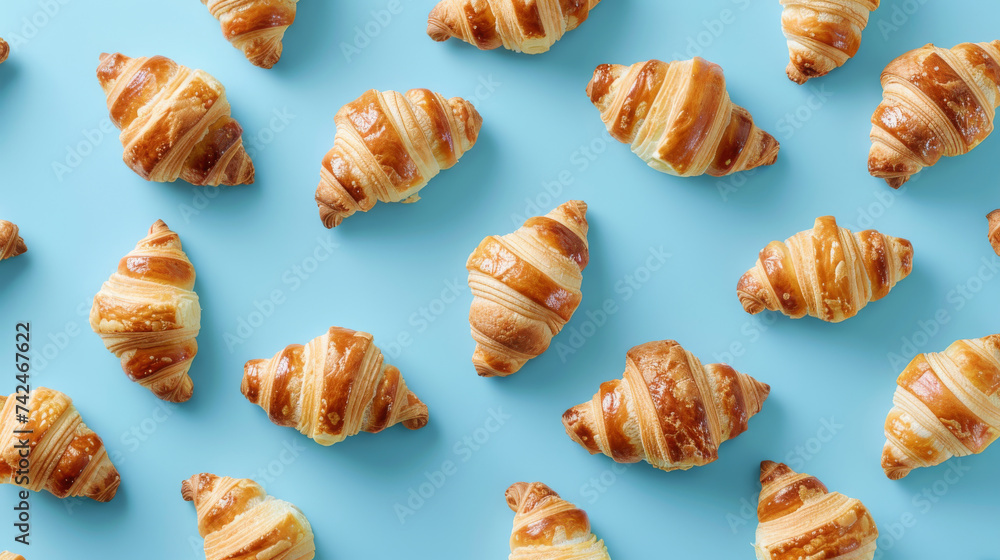 Patterned layout of freshly baked golden croissants on a blue background from an overhead perspective. Patterned layout of freshly baked golden croissants on a blue background from an overhead perspective.