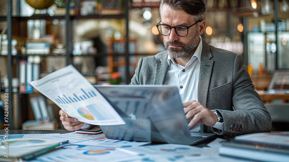 Businessman analyzes documents. He uses his laptop for maximum productivity while working on charts and documents. Businessman analyzes documents. He uses his laptop for maximum productivity while working on charts and documents.