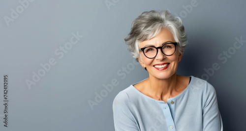 Mujer mayor sonriente con gafas fondo gris azul photo