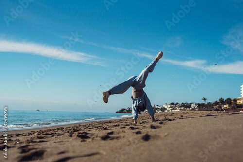 A tanned young woman jumps in a blue suit, a brunette in a tracksuit, an active girl jumps cheerfully on the sea coast. Athletic girl in a tracksuit jumping on the sand