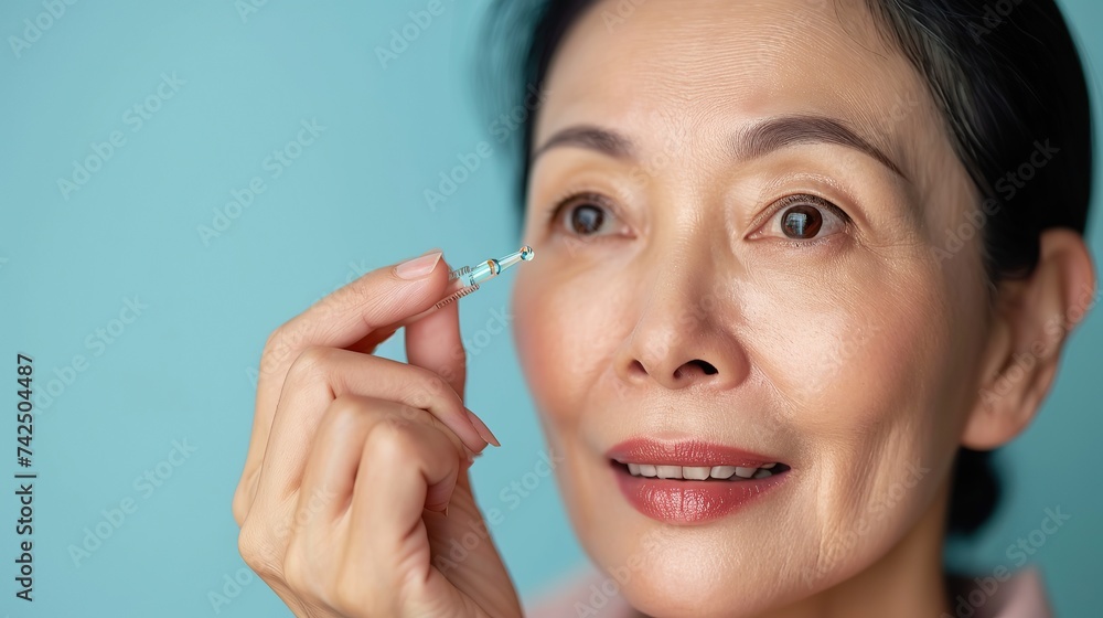 Closeup cut portrait of senior mature older Asian woman putting drop of antiaging pipette serum essence oil on finger hand. copy space for text. Closeup cut portrait of senior mature older Asian woman putting drop of antiaging pipette serum essence oil on finger hand. copy space for text.