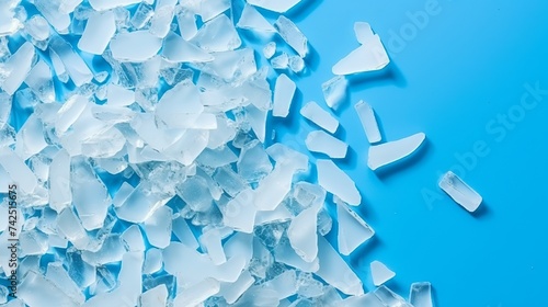 Top view of pile of broken white small glass pieces on blue background. Sharp glass fragments ready to be remelted