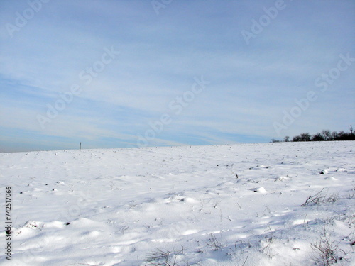 An amazing natural picture of a combination of the bright white color of the snowy steppe and the sunny white-blue sky in the frosty winter.
