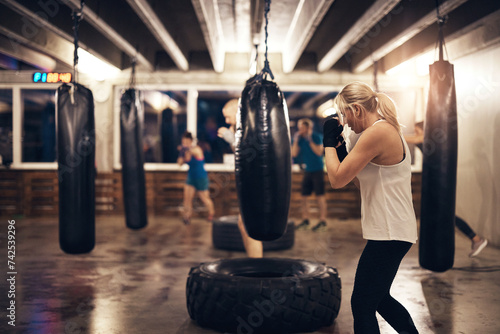 Fit woman working out with a punching bag in a boxing gym class photo