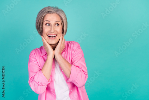 Photo of happy elderly business woman in pink trendy shirt looking empty space and touch neck isolated on aquamarine color background