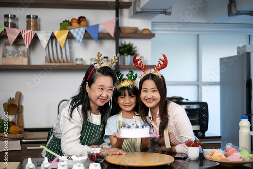 Asian little girl make a wish and blowing candles on cake with grandmother and mother in kitchen room at home. Family celebrating at home.Cheerful little girl celebrate birthday party with her parents