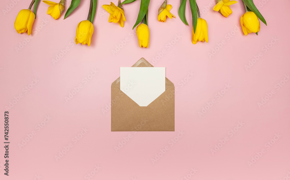 Top view of yellow tulips and daffodils on pink background. Kraft envelope, white card. Spring colourful composition, flat lay, copy space. Top view of yellow tulips and daffodils on pink background. Kraft envelope, white card. Spring colourful composition, flat lay, copy space.