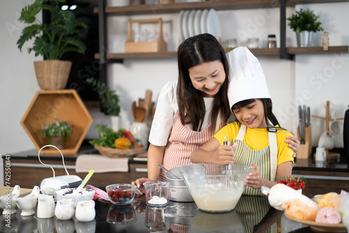 A little girl helping mother preparation baking in holidays. Mother teaching little daughter how to mix flour for baking cookies in kitchen at home. Children learning cooking concept