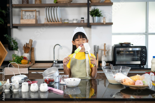 Asian little girl in apron and chef hat holding kitchen equipment on hands smiling to camera in kitchen. Child practicing to be a chef. Children dream careers. Concept for cooking learning for kid