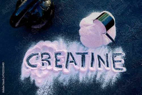 Strawberry creatine powder on a dark table with the word creatine written on it. This composition is accompanied by a scoop and a kettlebell.