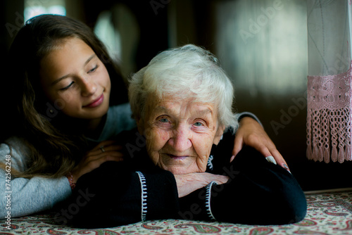 A little girl hugs her old grandmother. The old woman looks at the camera.