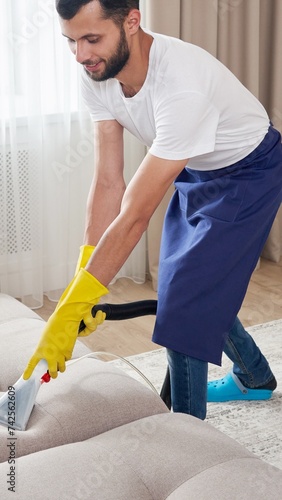 Close-up of housekeeper holding modern washing vacuum cleaner and cleaning dirty sofa with professionally detergent. Professional springclean at home concept photo