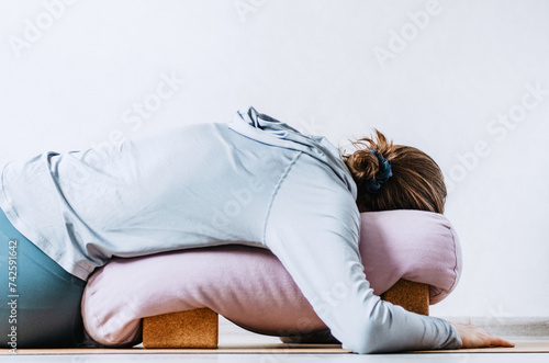 Photos Woman doing restorative yoga twist with bolster on cork blocks