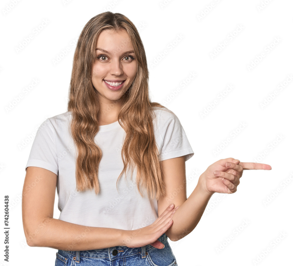 Obraz premium Studio portrait of a blonde Caucasian woman smiling cheerfully pointing with forefinger away.