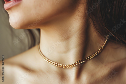 Close-up of a young woman wearing an elegant golden chain necklace on a neutral background