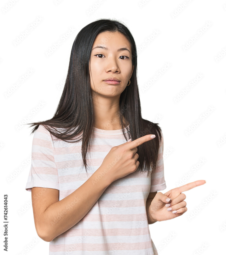 Young Chinese woman in studio setting shocked pointing with index fingers to a copy space. Young Chinese woman in studio setting shocked pointing with index fingers to a copy space.
