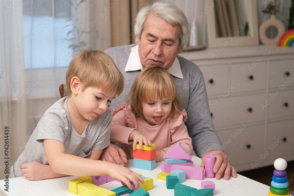 Grandfather playing toys with grandson and young granddaughter indoor. Old man grandpa studying with his grandchildren at weekend. Senior male having fun with kids. Happy multigeneration family video Grandfather playing toys with grandson and young granddaughter indoor. Old man grandpa studying with his grandchildren at weekend. Senior male having fun with kids. Happy multigeneration family video