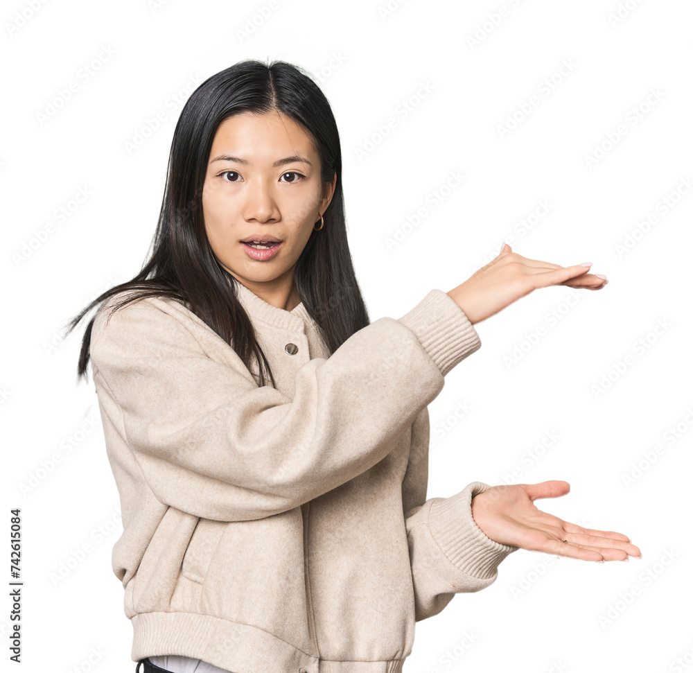 Young Chinese woman in studio setting shocked and amazed holding a copy space between hands. Young Chinese woman in studio setting shocked and amazed holding a copy space between hands.