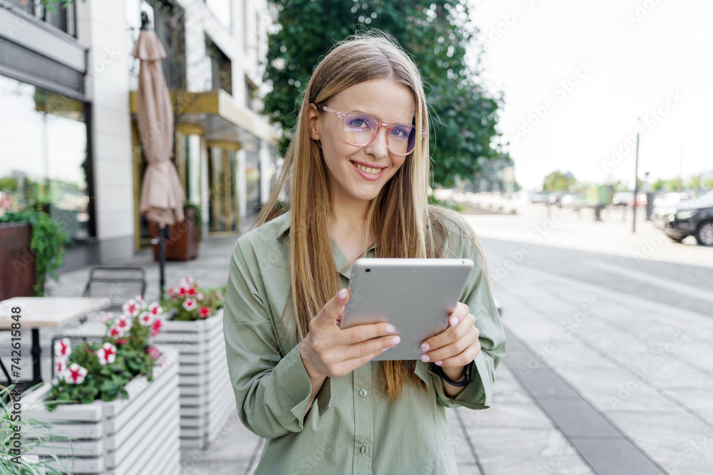 Urban professional woman using a tablet, smiling on a city street with flowers. Urban professional woman using a tablet, smiling on a city street with flowers.