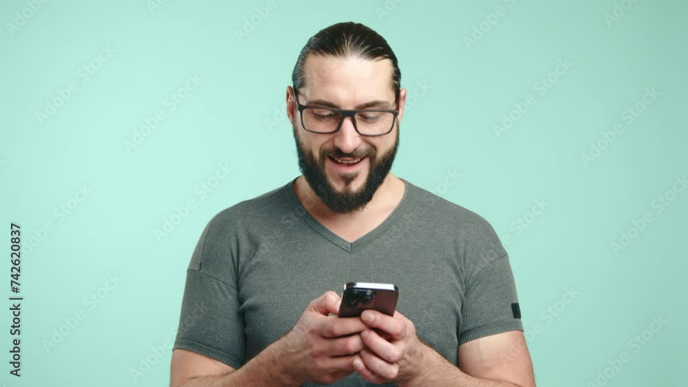A mature man with a well-groomed beard carefully adjusts his stylish glasses, staring confidently into the camera lens against a uniform light blue background. Camera 8K RAW. A mature man with a well-groomed beard carefully adjusts his stylish glasses, staring confidently into the camera lens against a uniform light blue background. Camera 8K RAW.