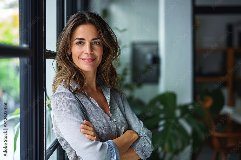 Smiling confident Latin professional mid aged business woman corporate manager leader, happy beautiful 40s mature female executive standing at office window arms crossed looking at camera,GenerativeAI
