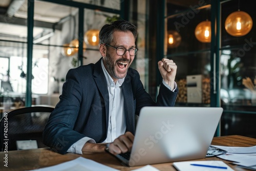 Happy successful mid aged business man investor wearing suit celebrating success in office looking at laptop rejoicing online investment financial win, Generative AI © Media Masterpieces