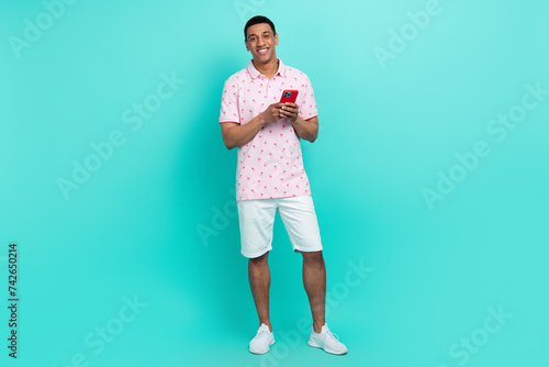 Full length photo of intelligent man wear print t-shirt white shorts holding smartphone read email isolated on turquoise color background