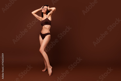 No retouch full body photo of sexy woman wear lingerie touching hair stand near logo empty space isolated on dark brown color background