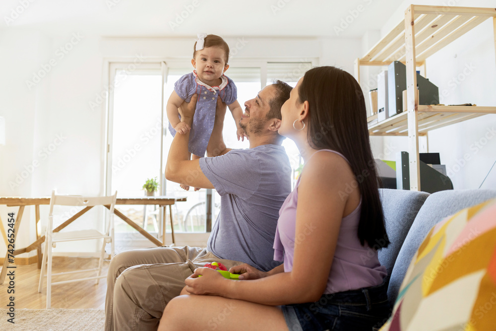 cheerful baby playing with his dad while holding him up pretending to fly. Having fun together with mom by the side cheerful baby playing with his dad while holding him up pretending to fly. Having fun together with mom by the side