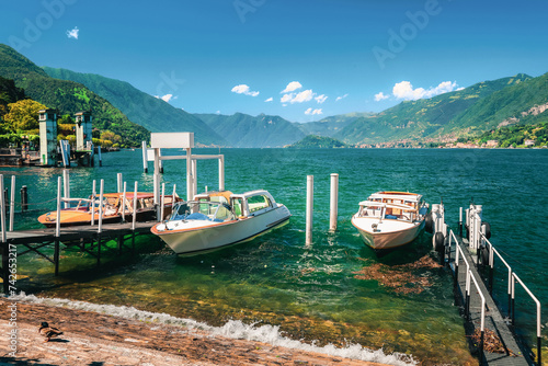 Lake Como (Italian Lago di Como) in summer. Docked motor boats and yachts at pier. Colorful landscape, Alps mountains and blue water. Fashionable vacations in Bellagio, Italy.