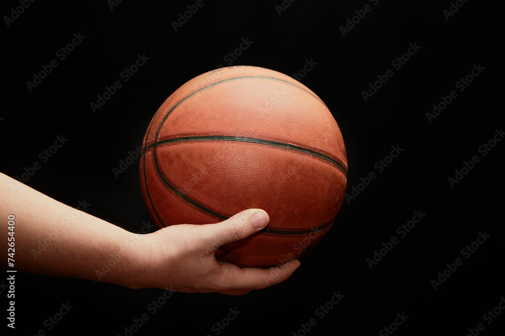 hand holds a lit basketball on a black background, close-up, the start of the game, sports background