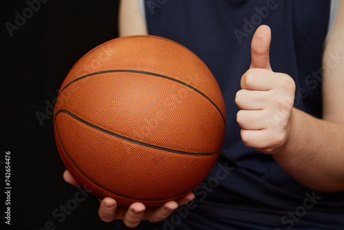 basketball player’s hand holding a basketball with one hand, and the other hand showing a thumbs up. Sports victory in basketball, invitation to a basketball match © Александр Ланевский