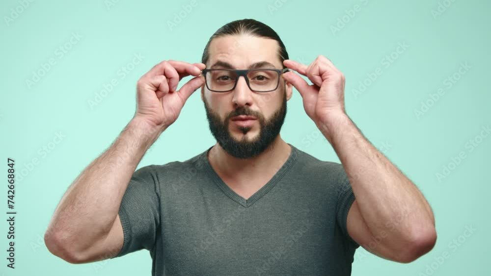 A stylish and thoughtful male with a neat beard carefully adjusting his trendy eyeglasses, gazing confidently into the camera on a subtle blue backdrop. Represents the blend of fashion and vision. A stylish and thoughtful male with a neat beard carefully adjusting his trendy eyeglasses, gazing confidently into the camera on a subtle blue backdrop. Represents the blend of fashion and vision.