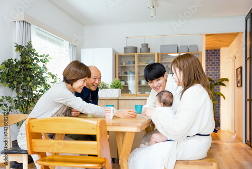 自宅で孫の赤ちゃんをあやす祖父と祖母（3世帯家族のイメージ）