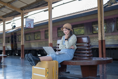 Girl using a laptop while waiting in a train station, Girl on train station with luggage working on laptop computer, laptop in use, sits with a suitcase
