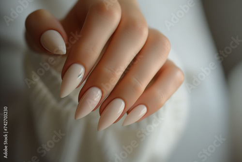 A young woman hand with a beige manicure and a white blouse