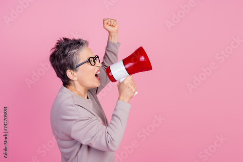 Profile side photo of confident retired woman hold bullhorn say tell announce information empty space isolated on pink color background