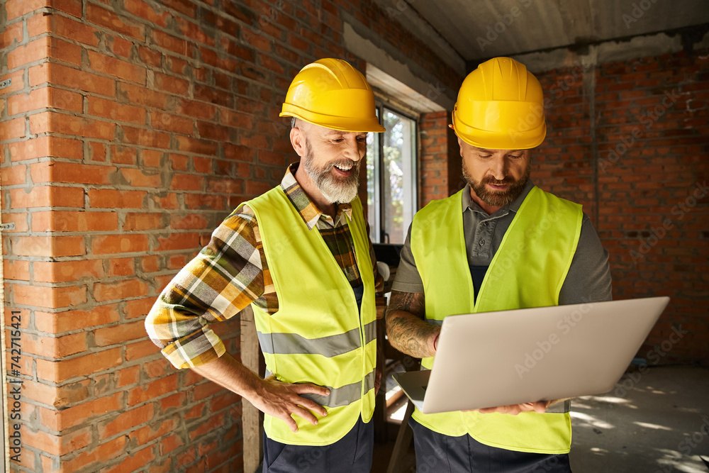 cheerful devoted construction workers in safety vests working with laptop on site, cottage builders cheerful devoted construction workers in safety vests working with laptop on site, cottage builders