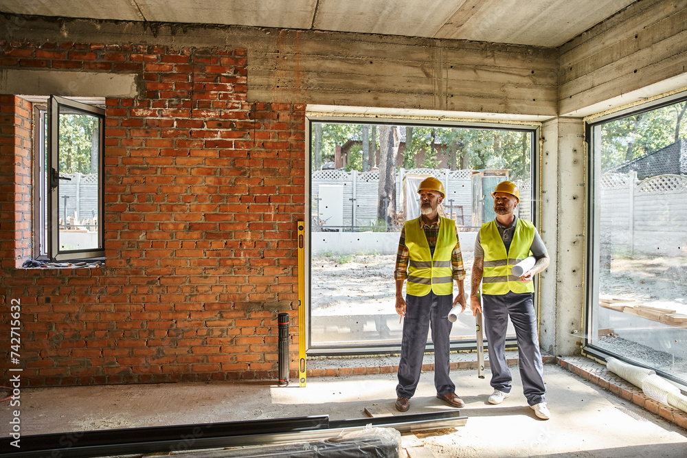dedicated men in safety vests and helmets holding blueprints on construction site, cottage builders dedicated men in safety vests and helmets holding blueprints on construction site, cottage builders