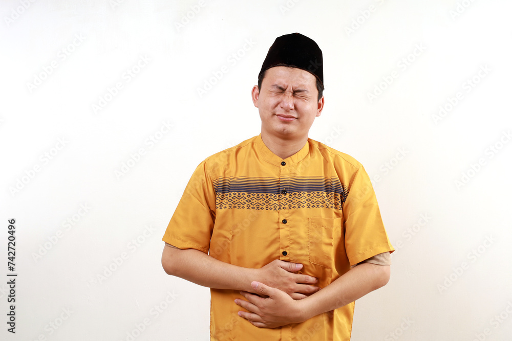 Asian muslim man squeeze his stomach for having stomachache pain, against white background Asian muslim man squeeze his stomach for having stomachache pain, against white background