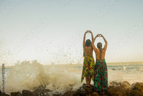 pareja de espaldas frente al mar haciendo corazón con sus manos 
