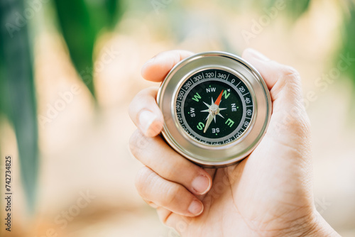 A traveler hand holds a compass in a park representing the search for direction and guidance. Amidst nature beauty the compass signifies exploration and discovery.